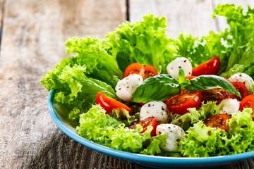 Salad with mozzarella cheese and cherry tomatoes on wooden table