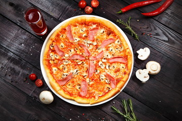 italian pizza with cheese mushrooms ham chili peppers and tomatoes on the black wooden background