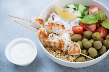 Close-up of greek food bowl with quinoa, souvlaki and vegetables over light-blue stone background, studio shot