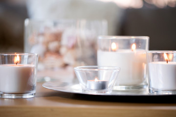 decoration, hygge and cosiness concept - burning white fragrance candles on tray on table
