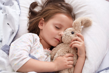Close up portrait of little girl hugging her teddy bear and being happy, having rest after interesting day in kinder garten. Concept of: relax, love, childhood, sleep and wake up in morning.