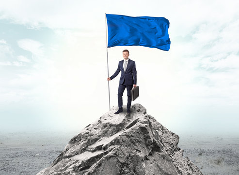 Handsome businessman on the top of the mountain with blue flag