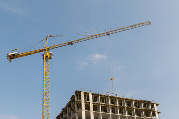 A high-rise construction crane against the sky is building a multi-storey building using modern technology from metal, concrete and brick, which will become an apartment building or office center