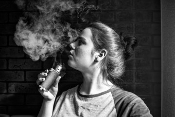 Vape teenager with  problem skin. Portrait of young cute girl smoking an electronic cigarette in the bar. Bad habit that is harmful to health. Vaping activity. Black nad white.