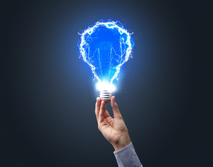 Hand holding shiny light bulb on dark background. New idea concept