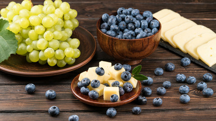 .cheese and blueberries and grapes on a wooden background
