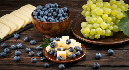.cheese and blueberries and grapes on a wooden background