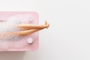 doll legs in pink bath on pastel background. creative minimalistic concept of relax. top view. 