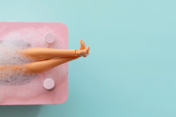 doll legs in pink bath on pastel background. creative minimalistic concept of relax. top view. 