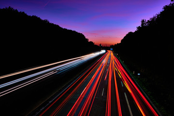 Auto Lichtspuren. Lichter auf der Autobahn. Spuren von Autos. Abstraktes Licht, Lichtschweife. Autbahn bei Sonnenuntergang und viel Verkehr. Autobahn bei Nacht.