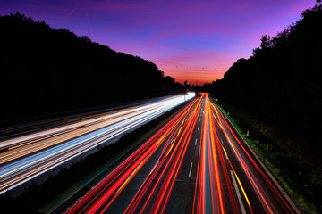 Auto Lichtspuren. Lichter auf der Autobahn. Spuren von Autos. Abstraktes Licht, Lichtschweife. Autbahn bei Sonnenuntergang und viel Verkehr. Autobahn bei Nacht.