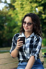girl drinks coffee from a disposable cup in the park on a bench