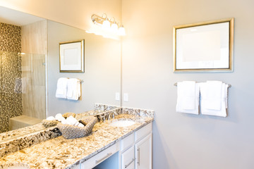 Hand towels in woven basket in bathroom granite countertop with sink and mirror in staging model...