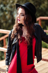 Bright portrait of brunette woman in a red dress and black jacket posing on nature. Fashion beauty photo