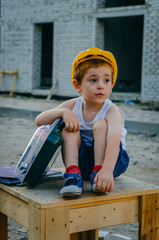 Children's role-playing games - a profession builder. Early development of the child, ideas for the game. A boy in a protective helmet with a suitcase with tools at a construction site.