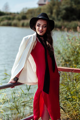 Bright portrait of brunette woman in a red dress and white jacket posing on nature. Fashion beauty photo