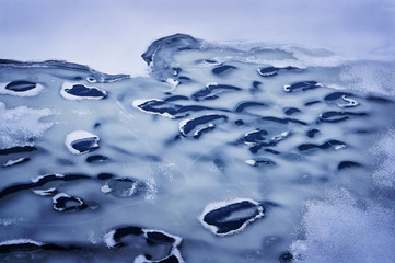 Winter backdrop of lake covered by melting ice and snow and airholes with dark blue water