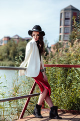 Bright portrait of brunette woman in a red dress and white jacket posing on nature. Fashion beauty photo