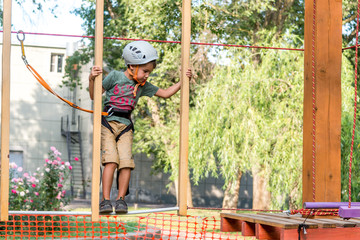 Rope Park-climbing center. Walking in protective equipment. Baby boy playing in adventure Park passes obstacles. Extreme children's leisure and entertainment. Sports are for the nimble and the bold.