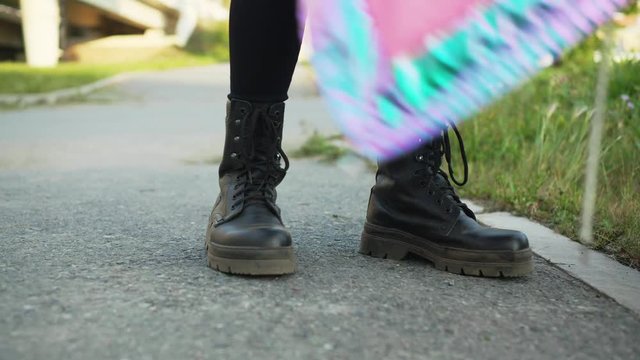 Female legs wearing black leather boots standing on asphalt road at summer. Girl in leather shoes walking on green grass in city park
