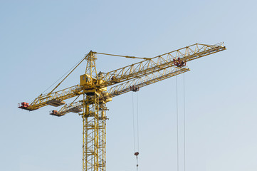 A yellow high-rise building crane against a blue sky builds multi-storey apartment buildings using modern technologies of metal, concrete and brick according to an architectural project