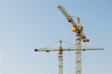 Naklejka premium A yellow high-rise building crane against a blue sky builds multi-storey apartment buildings using modern technologies of metal, concrete and brick according to an architectural project