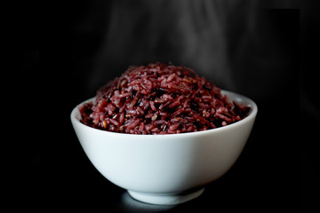 The hot stream brown rice berry in the white bowl isolated on black background