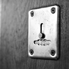 chrome keyhole in wooden door closeup, black and white photo.