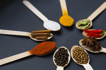 circular composition of assorted spices in wooden spoons on a dark background. black peppercorns and coriander in the front. close up