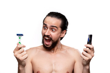 Bearded man with mustache chooses between electric razor and old shaving stick standning bare...