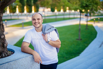 Portrait of a smiling bald handsome man of 30 years old in a modern park with a jacket in his hands