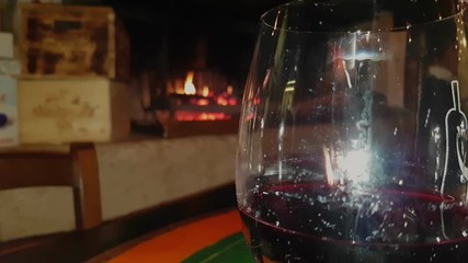 Close up of glass of red wine with a fireplace in the background with fire, Vittorio Veneto, Italy