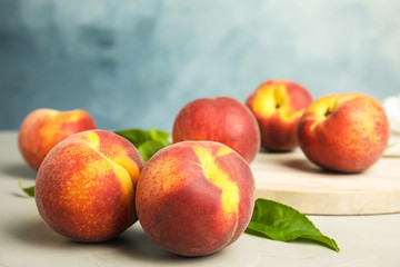 Fototapeta na wymiar Tasty fresh peaches with leaves on grey table against blue background