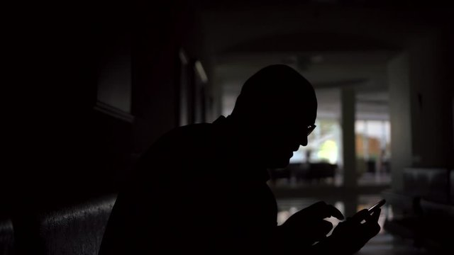 bald man silhouette types on smartphone sitting in dark hall