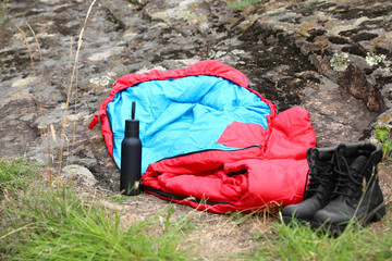 Sleeping bag, boots and bottle outdoors. Camping gear
