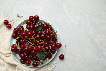 Plate of tasty cherries and fabric on grey marble table, flat lay with space for text