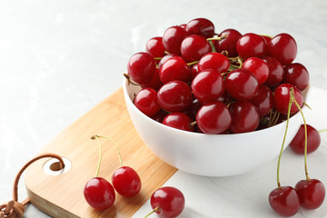 Wooden board with bowl of tasty ripe cherries on light table