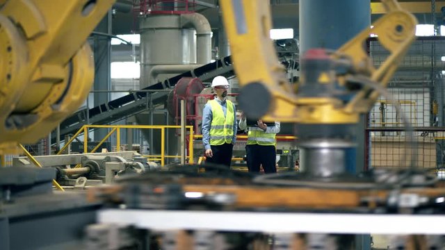 Workers, factory colleagues stand in a facility while a machine works with bricks.
