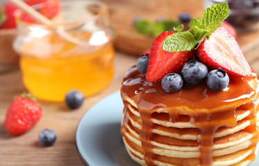 Delicious pancakes with fresh berries and syrup on wooden table, closeup