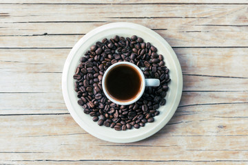 Hot Espresso in white cup and roasted coffee beans on a wooden table, top view