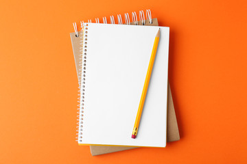 Notebooks with pencil on orange background, top view - Powered by Adobe