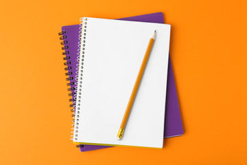 Notebooks with pencil on orange background, top view