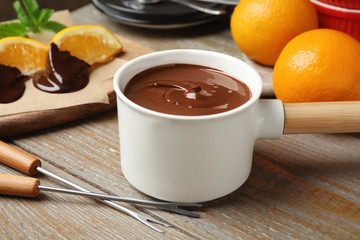 Fondue pot with milk chocolate and oranges on wooden table, closeup