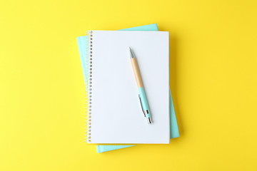 Notebooks and pen on yellow background, top view