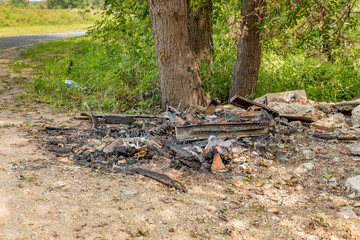 Trash and garbage illegally dumped along the side of a road by a river and burned, leaving behing a pile of charred debris, metal, and wire