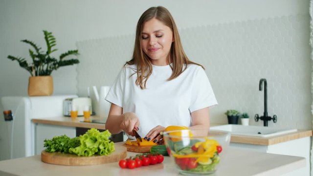 Portrait of beautiful young housewife cooking vegetable salad slicing pepper with knife in kitchen busy with cookery. People, lifestyle and home-made food concept.