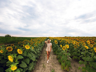 Fototapeta premium Beautiful young woman walking through sunflower field