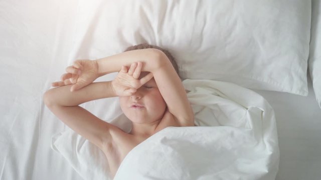 Top view of a young boy yawning and stretching arms in bed