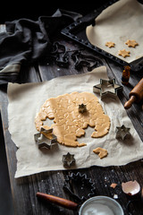 process of baking christmas gingerbread cookies on baking tray with parchment on rustic wooden table with rolling pin, flour and cookie cutters