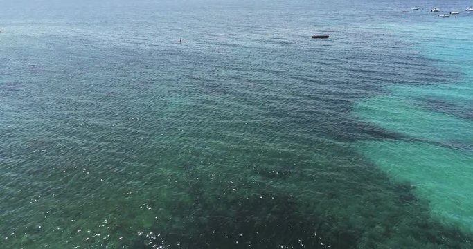 Aerial top view pan shot of clear unpolluted turquoise sea with sun rays. Green seaweeds on the bottom and a conoe. Summer holidays and vacation. Travel to the beach.